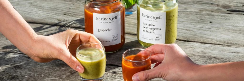 visuel d'ambiance été — table dressée fraîche, bocal de gaspacho servi dans un verre avec glaçons, terrasse.